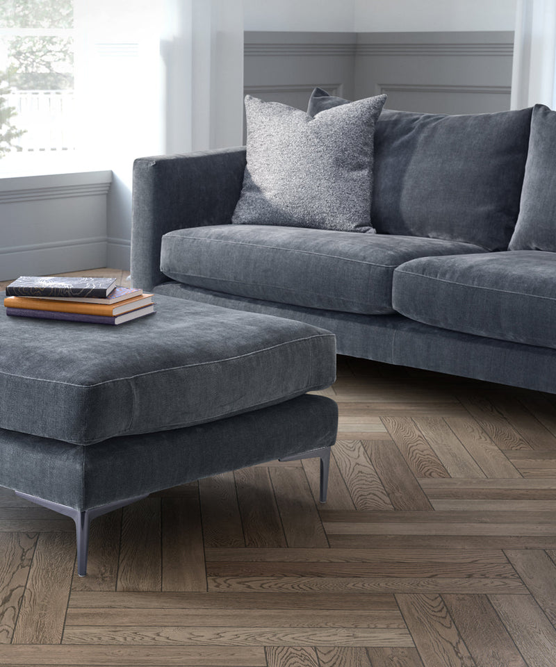 Featuring the Darwin footstool in a blue upholstery on a herringbone wooden floor