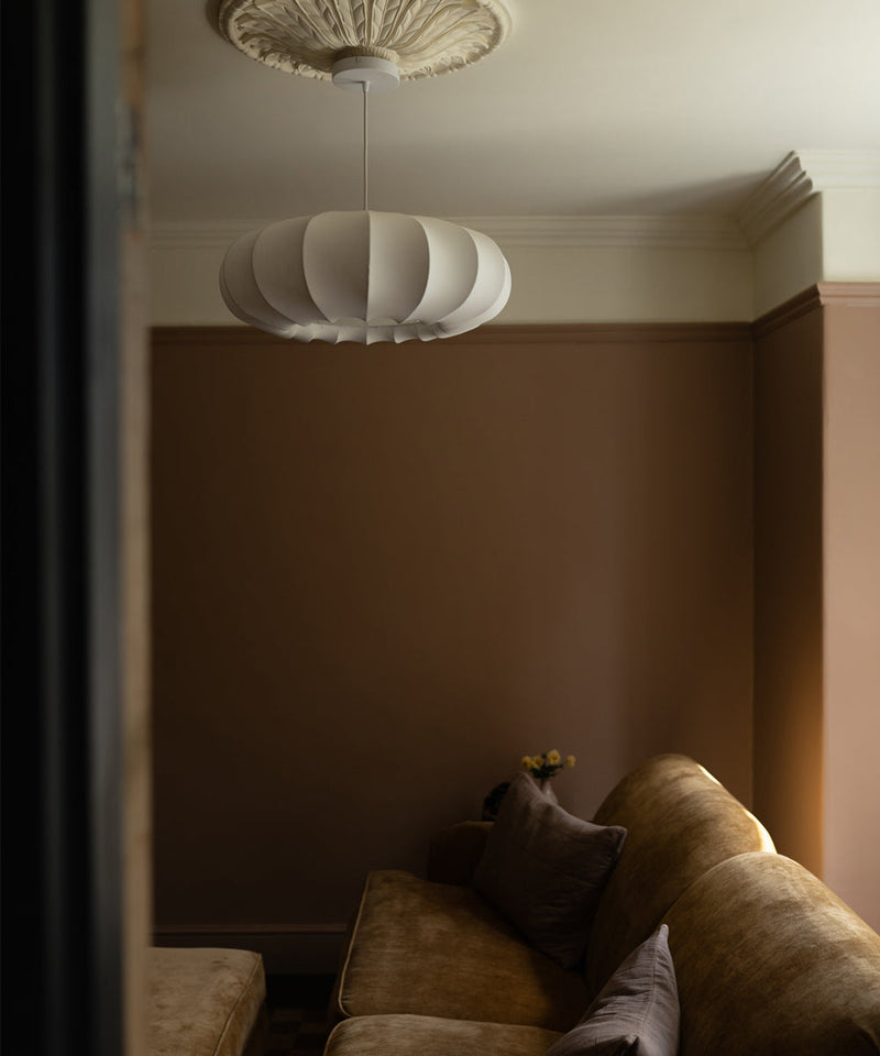 A living room with a neutral warm wall light and a Fibre 60 pendant hanging above a sofa