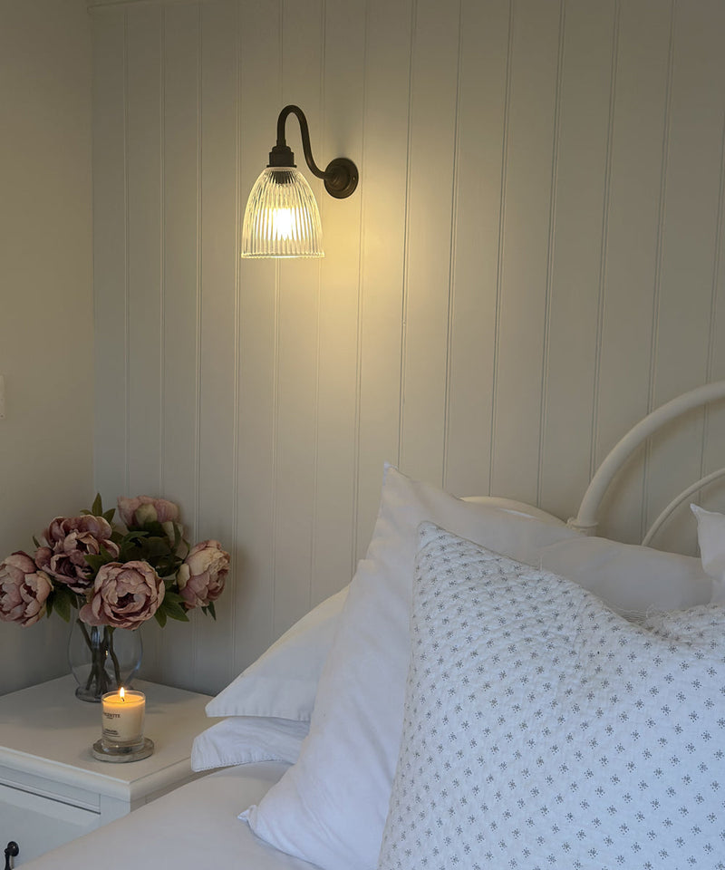 A wall night next to a bed and above a bedside table