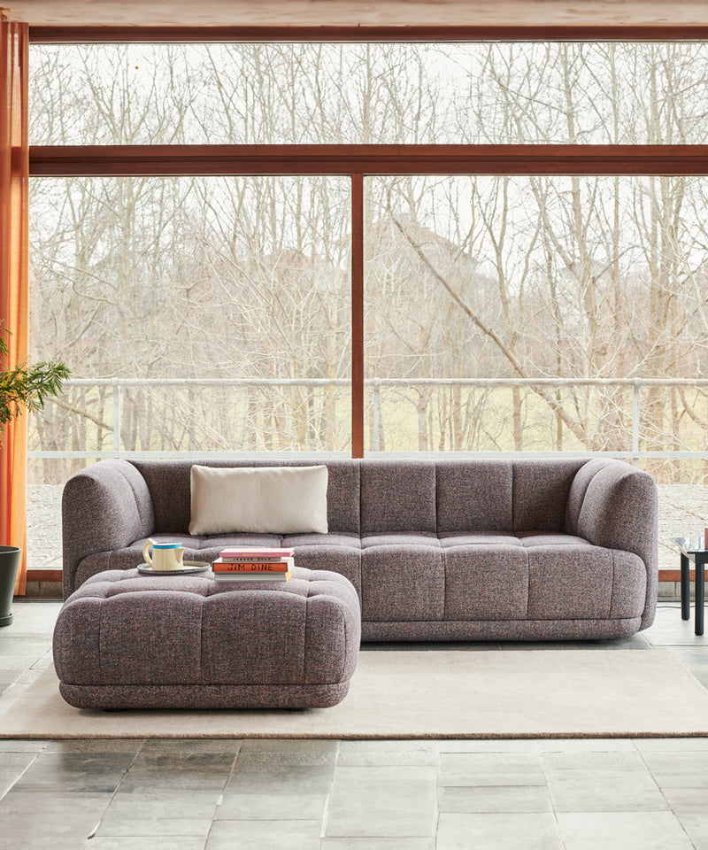HAY Quilton Sofa with matching ottoman in front  of a big window in an open plan living room