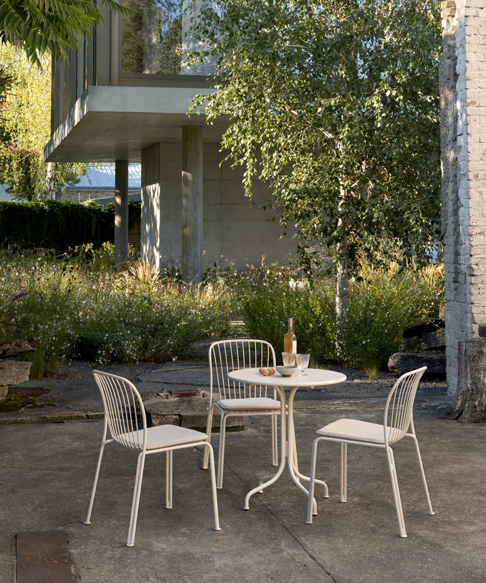 Thorvald Garden seating and a small table all finished in a bright white on a concrete patio outside a large modern home