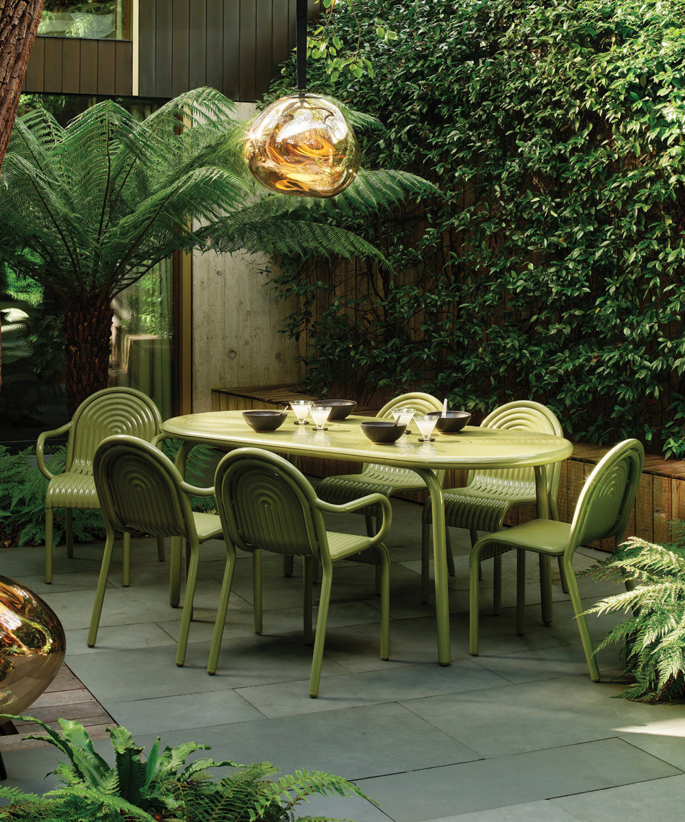 Featuring a green garden with trees and plants around a large patio with  a furniture dining set in the centre