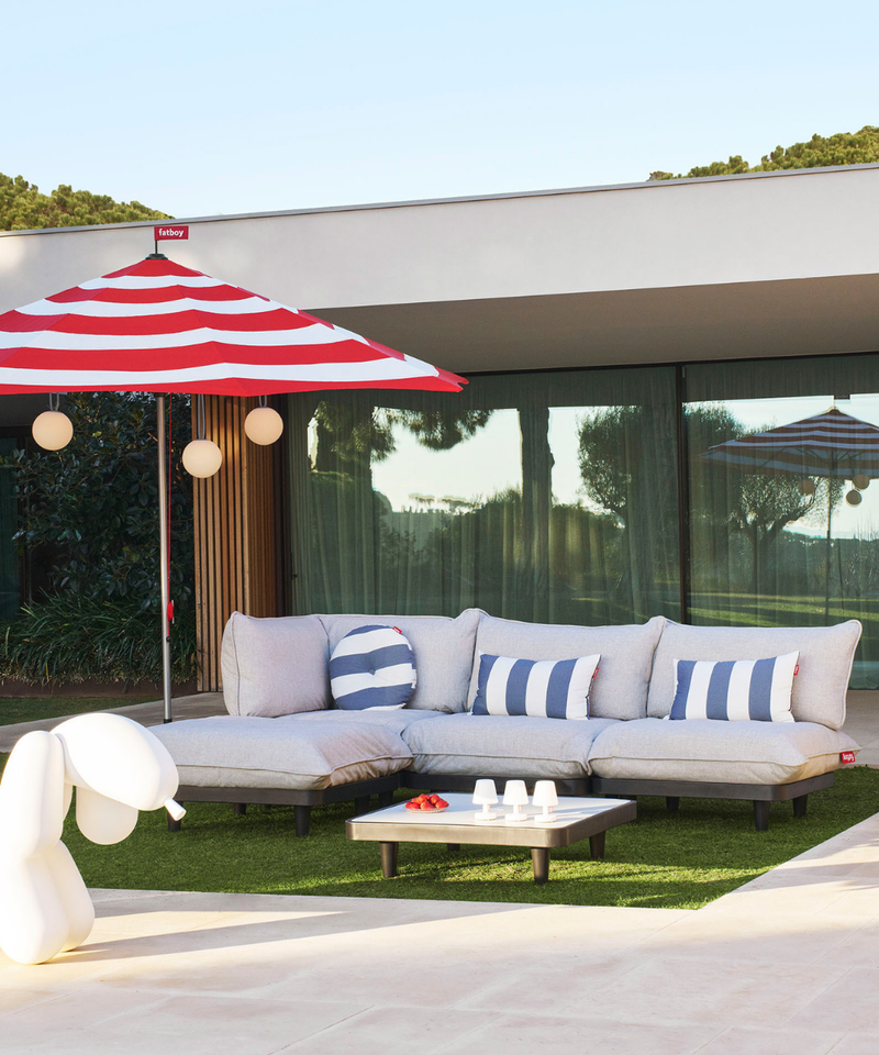 Modern garden setup featuring the Fatboy Paletti outdoor sofa, Fatboy red and white striped parasol  and Fatboy Bolleke Portable Garden Lights